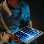 A child engrossed in using a digital tablet at night, illuminated by screen light.
