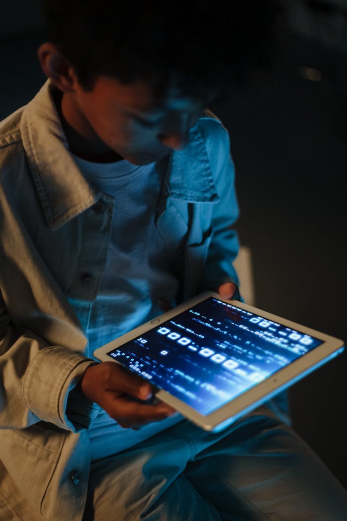 A child engrossed in using a digital tablet at night, illuminated by screen light.