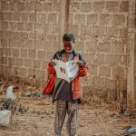 A young boy in Geidem, Nigeria, reads a newspaper outdoors, symbolizing curiosity and learning.