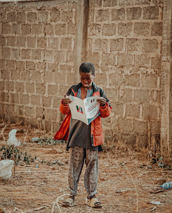 A young boy in Geidem, Nigeria, reads a newspaper outdoors, symbolizing curiosity and learning.